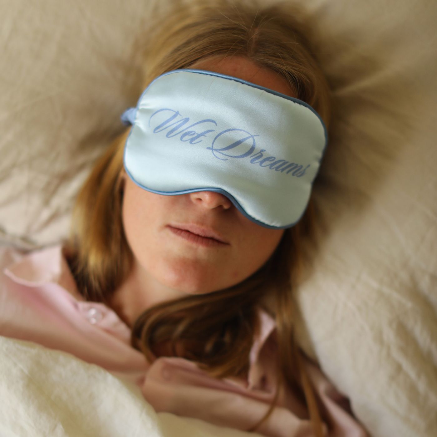 Blå natmaske, kan også bruges som blindfold med teksten Wet Dreams på, på kvinde der ligger i seng